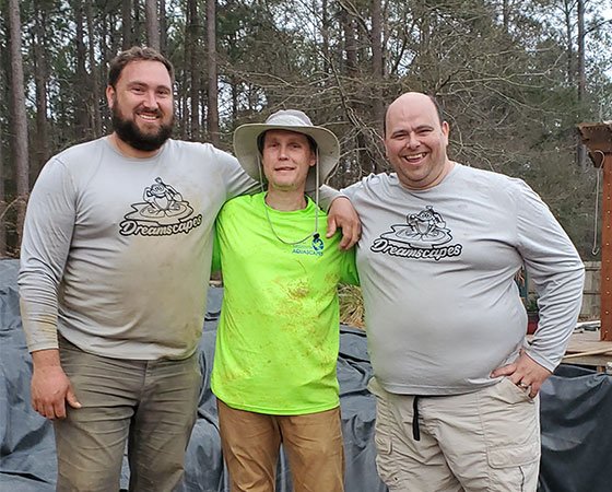 Three men outdoors, smiling, in casual work attire.