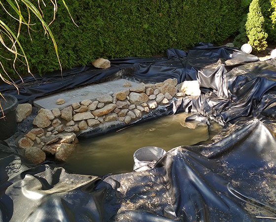 Partially constructed backyard pond with stones and liner