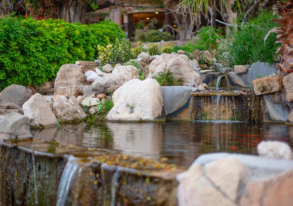 Small garden waterfall with rocks and greenery.