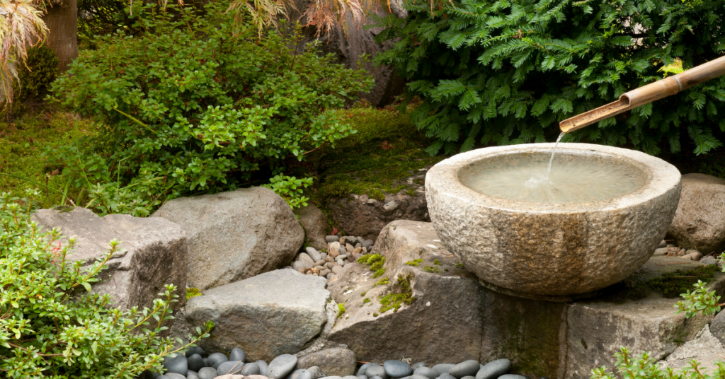 Stone bowl fountain by bushes and rocks