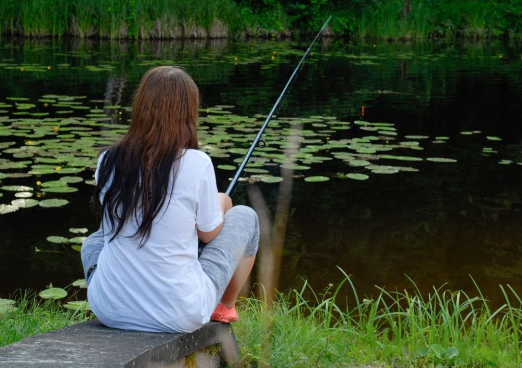 Woman fishing by pond with water lilies.